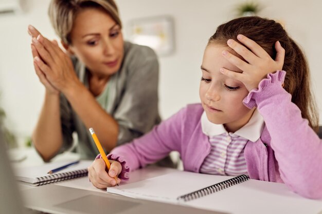 Petite fille écrivant dans un cahier tout en faisant ses devoirs avec l'aide de sa mère