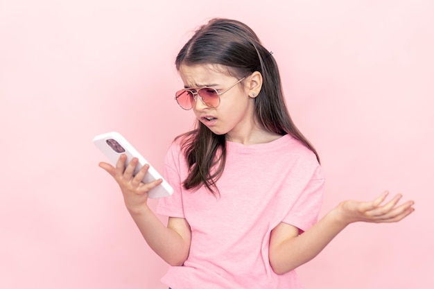 Petite fille élégante avec un smartphone sur fond rose