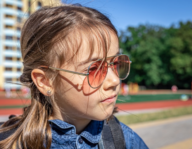 Petite fille, élève du primaire à lunettes de soleil, gros plan extérieur.