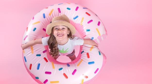 Une petite fille enfant en tenue décontractée allongée sur un cercle gonflable en forme de beignet. Fond rose. Vue de dessus. Concept d'été.