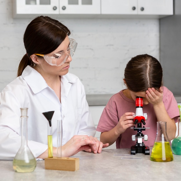 Photo gratuite petite fille et enseignante faisant des expériences scientifiques au microscope