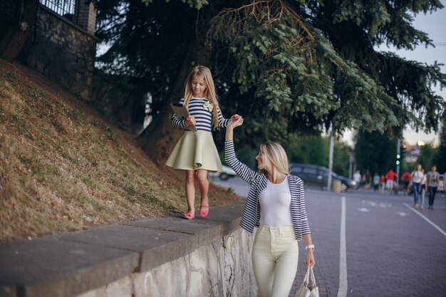 Petite fille escaladant un mur de pierre tout en saisissant la main de sa mère