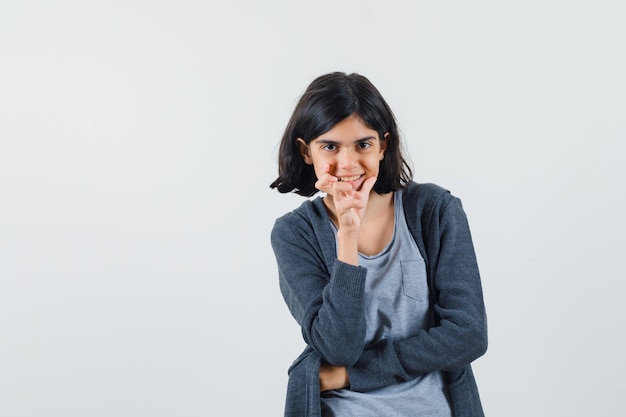 Petite fille étayant le menton sur place en t-shirt, veste et à l'optimiste.