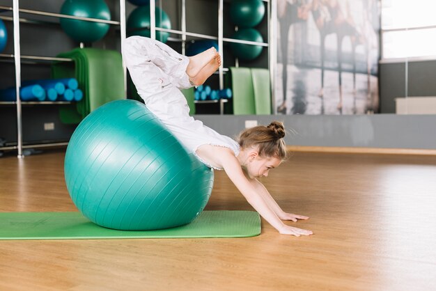 Petite fille faire des exercices avec ballon dans la salle de fitness