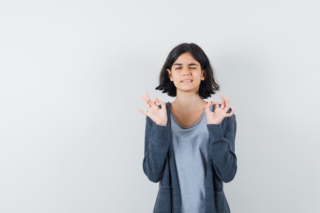 Petite fille faisant un geste de méditation en t-shirt, veste et à la confiance.