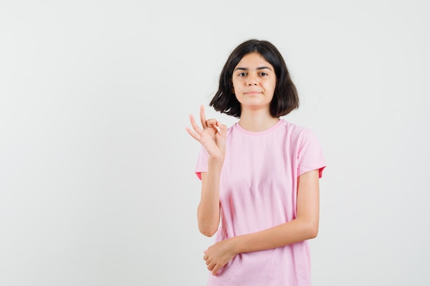 Petite fille faisant un geste ok en t-shirt rose et regardant confiant, vue de face.