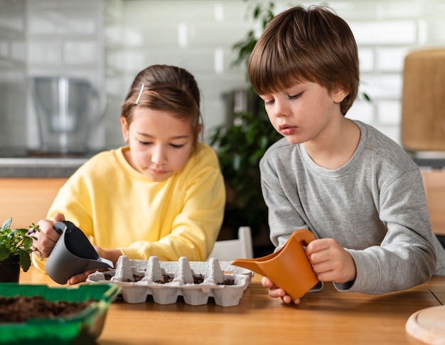 Petite fille et garçon arrosant les graines à la maison