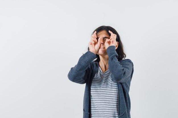 Petite fille en gardant les doigts croisés en t-shirt, veste et à la recherche d'espoir