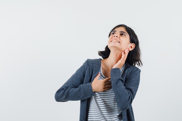 Petite fille gardant la main sur la poitrine en t-shirt, veste et à la joyeuse.