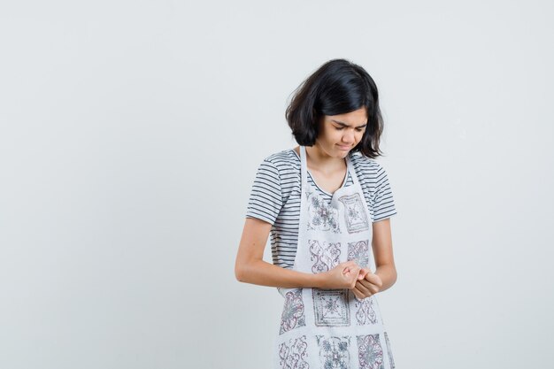 Petite fille gardant les poings serrés en t-shirt, tablier et à la recherche de reconnaissance.