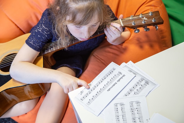 Une petite fille à la guitare apprend le solfège, les partitions et le solfège.