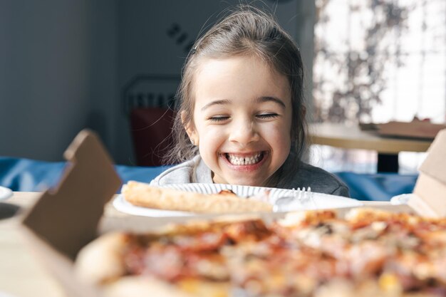 La petite fille heureuse regarde la pizza avec appétit