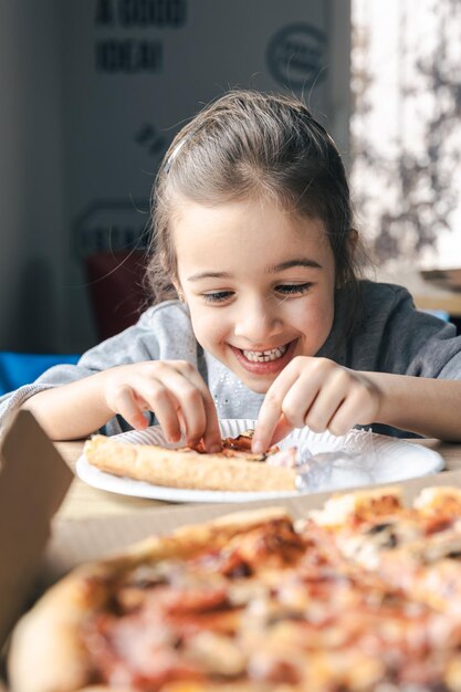 La petite fille heureuse regarde la pizza avec appétit