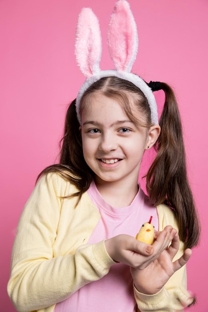 Photo gratuite une petite fille joyeuse présentant un jouet de poussin moelleux dans un studio rose