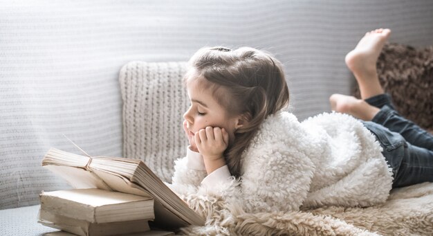 petite fille lisant un livre sur un canapé confortable, belles émotions