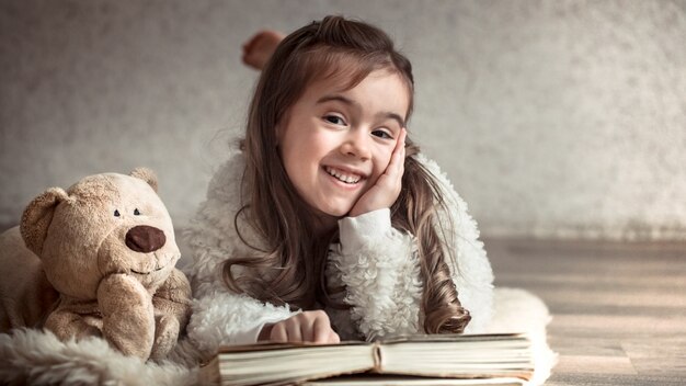 petite fille lisant un livre avec un ours en peluche sur le sol, concept de détente et d'amitié
