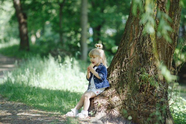 Petite fille mangeant une crème glacée se penchant sur un arbre