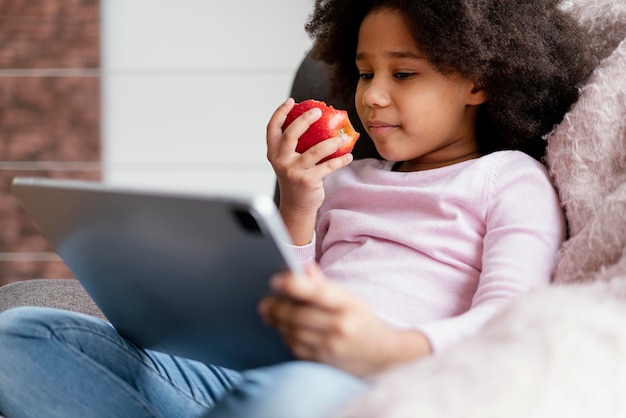 Petite fille mangeant des pommes et utilisant une tablette