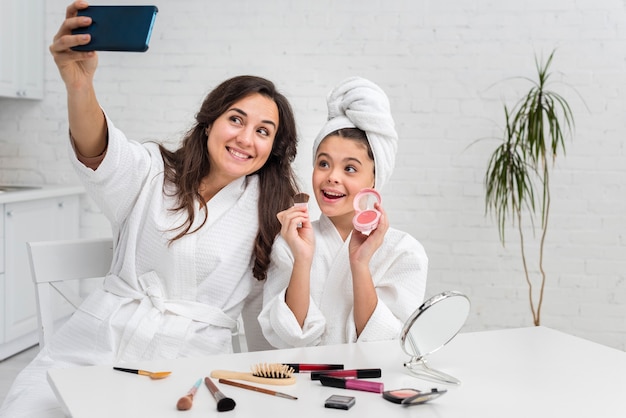 Petite fille et mère prenant un selfie tout en faisant leur maquillage