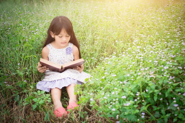 petite fille mignonne asiatique lisant livre à la nature.