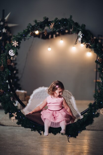 Une petite fille mignonne dans une robe avec des cruces d'ange est assise dans un grand paysage rond de branches d'épinette