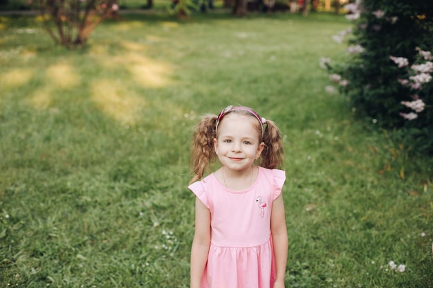 Une petite fille mignonne dans une robe rose dans un parc verdoyant au printemps ou en été