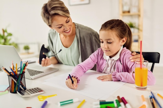 Petite fille mignonne écrivant des devoirs avec l'hép de sa mère