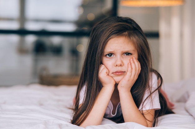 Petite fille mignonne avec un visage triste allongé sur le lit