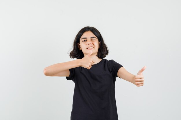 Petite fille montrant deux pouces vers le haut, un clin d'œil en vue de face de t-shirt noir.