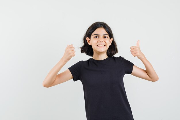 Petite fille montrant deux pouces vers le haut en t-shirt noir et à l'air heureux. vue de face.