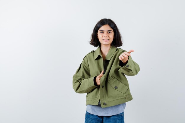 Petite fille montrant le geste de donner en manteau, t-shirt, jeans et jolie vue de face.