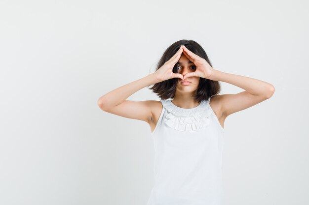 Petite fille montrant le geste du cœur en chemisier blanc, vue de face.