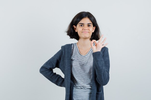 Petite fille montrant le geste ok en t-shirt, veste et à la confiance.