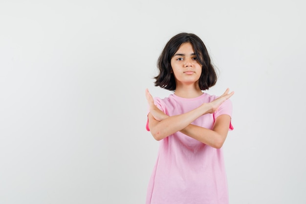 Petite fille montrant un geste de refus en t-shirt rose et à la recherche résolue. vue de face.