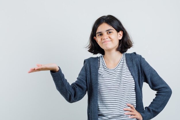 Petite fille montrant quelque chose ou accueillant en t-shirt, veste et à la bonne humeur