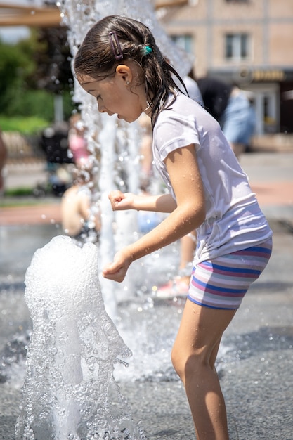 Une petite fille mouillée se rafraîchit dans une fontaine par une chaude journée d'été.