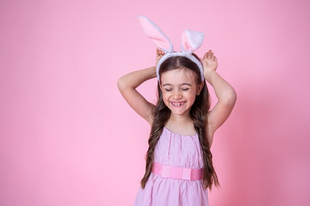 Petite fille avec des oreilles de lapin de Pâques posant sur un studio rose