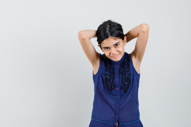 Petite fille organisant ses cheveux derrière la tête en chemisier bleu et à la belle. vue de face.