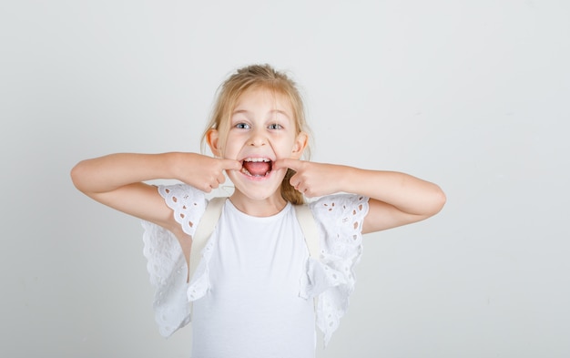 Petite fille ouvrant la bouche avec les doigts en t-shirt blanc et à la drôle.