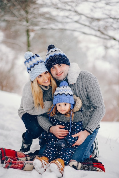 Petite fille avec des parents assis sur une couverture dans un parc d'hiver