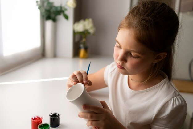 Petite fille peignant un vase à la maison