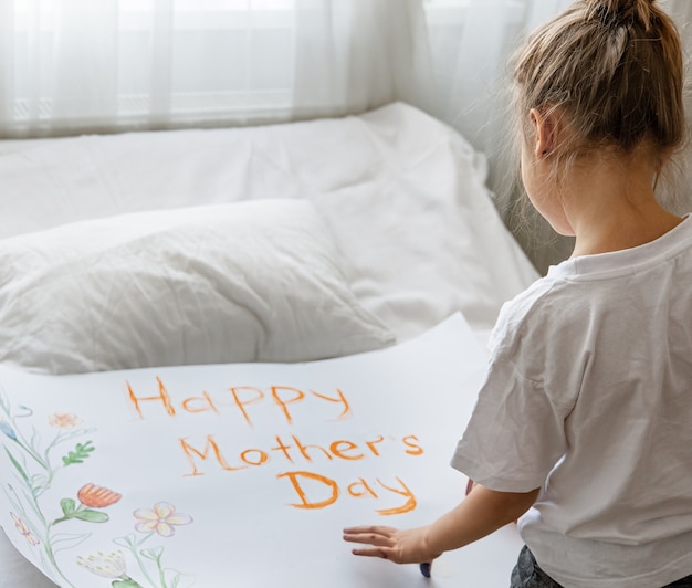 Petite fille peint une carte de voeux pour maman avec l'inscription Bonne fête des mères et fleurs.