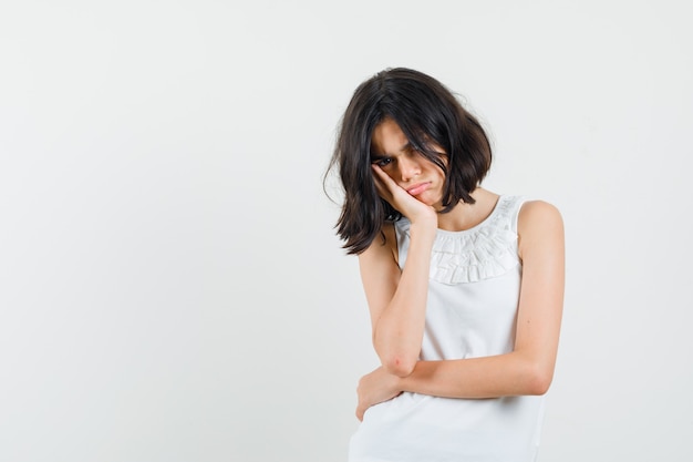 Petite fille penchée joue sur la paume surélevée en chemisier blanc et à la vue offensée, de face.