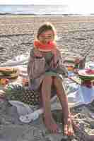 Photo gratuite une petite fille sur une plage de sable mange une pastèque