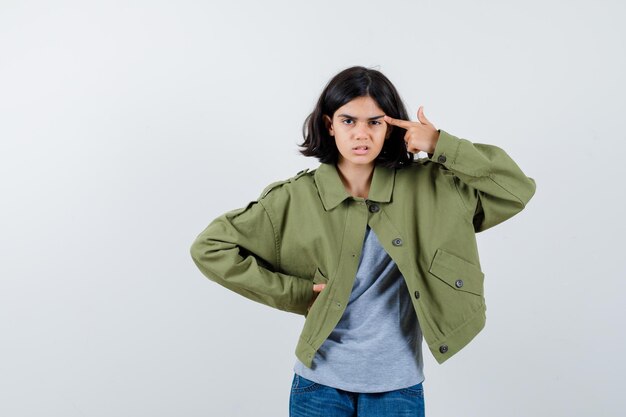 Petite fille pointant la tête dans un manteau, un t-shirt, un jean et l'air confiant. vue de face.