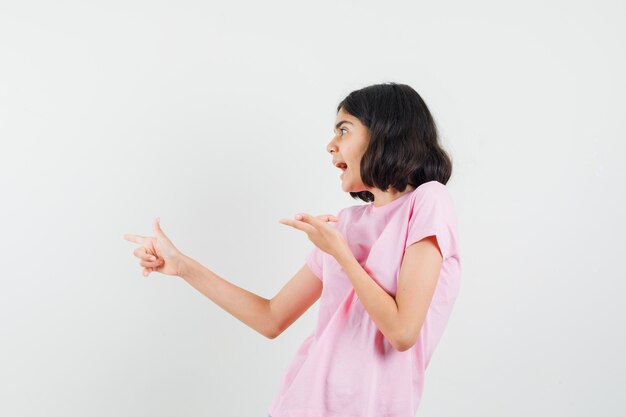 Petite fille pointant vers le côté en t-shirt rose et regardant étonné, vue de face.