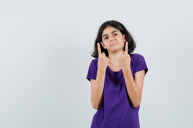 Petite fille pointant vers le haut en t-shirt et à la confusion.