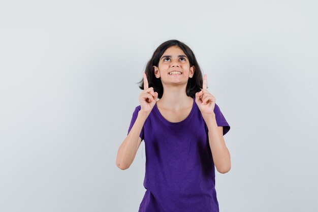 Petite fille pointant vers le haut en t-shirt et à la reconnaissance.