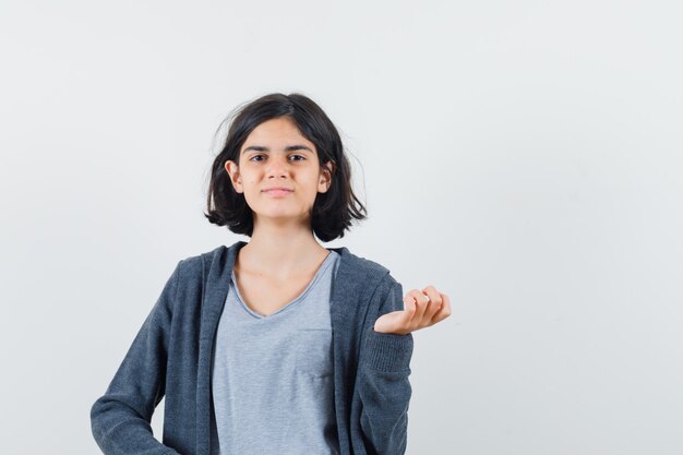 Petite fille posant debout en t-shirt, veste et à la vue confiante, de face.