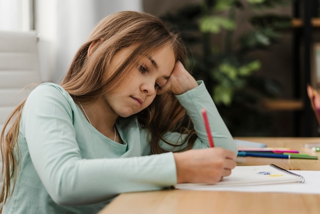 Petite fille prenant des notes tout en s'ennuyant à la maison